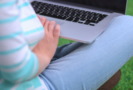 Young woman with laptop sitting on green grass . Portreit young womanの写真素材