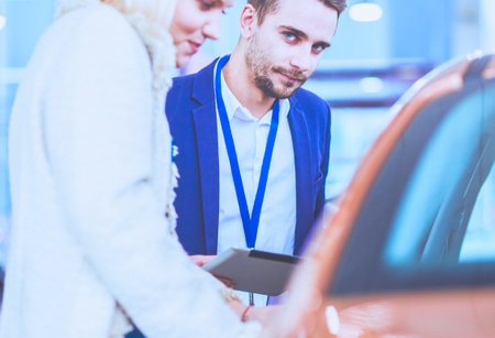 Dealer with woman stands near a new car in the showroomの写真素材