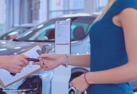 Car salesman sells a car to happy customer in car dealership and hands over the keysの写真素材