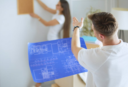 Woman helps her partner to hang painting on wall of their new house, she is framing the photo with her fingersの写真素材