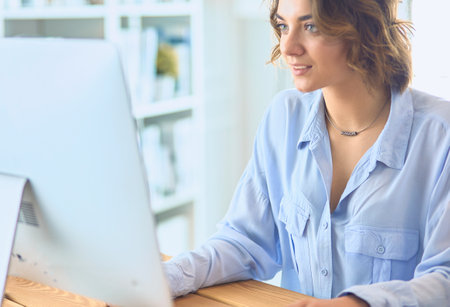 Pretty young woman sitting at desk and typing on laptopの写真素材