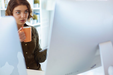 Attractive woman sitting at office desk, holding a cup of coffeeの写真素材