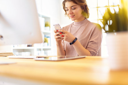 Young businesswoman text messaging while sitting at office in front of laptopの写真素材
