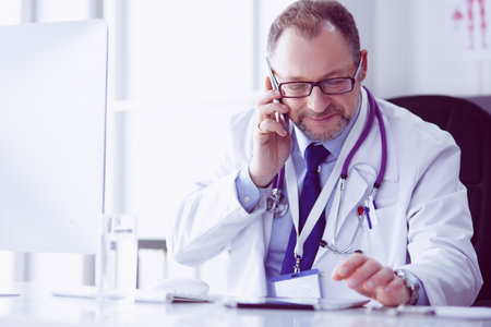 Portrait of senior doctor in office sitting at the deskの写真素材
