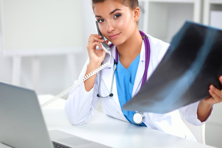 Young female doctor studying x-ray image sitting on the deskの写真素材