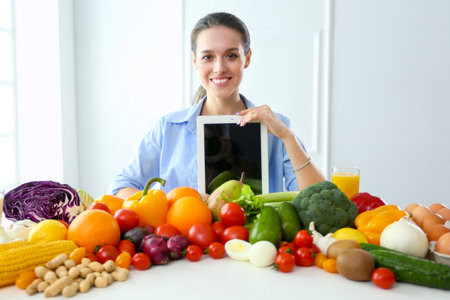 Young and cute woman sitting at the table full of fruits and vegetables in the wooden interior, holding tabletの写真素材