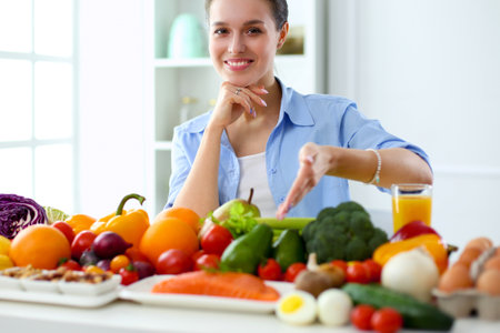 Young and cute woman sitting at the table full of fruits and vegetables in the wooden interiorの写真素材