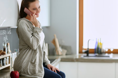 Young woman with orange juice and tablet in kitchenの写真素材