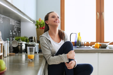 Young woman with orange juice and tablet in kitchenの写真素材