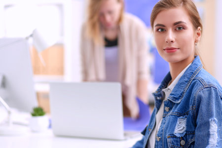 Two young woman standing near desk with instruments, plan and laptopの写真素材