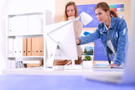 Two young woman standing near desk with instruments, plan and laptopの写真素材