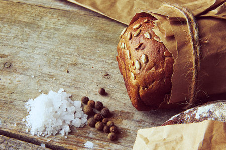 Two Loaves of Bread packed in paper on wooden table with salt and papper. Cropped photo.の写真素材