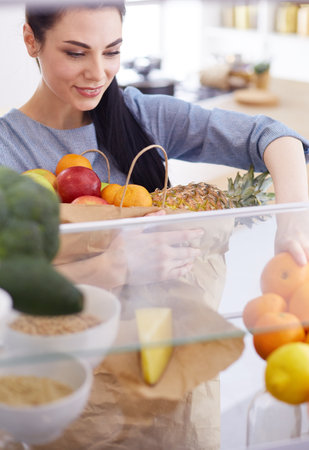 Smiling woman taking a fresh fruit out of the fridge, healthy food concept.の写真素材