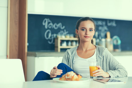 Young woman with orange juice and tablet in kitchenの写真素材