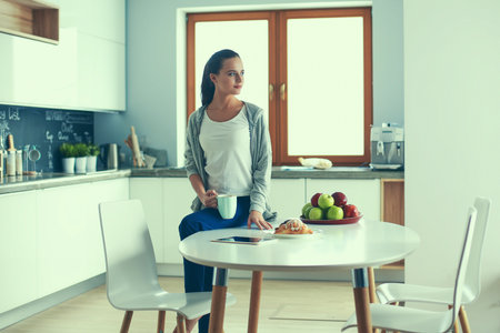Happy woman drinking tea in the kitchen at homeの写真素材