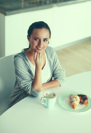 Woman drinking tea with sweet croissant at the kitchen tableの写真素材