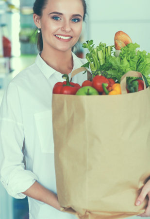 Young woman holding grocery shopping bag with vegetables .Standing in the kitchenの写真素材