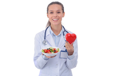 Portrait of a beautiful woman doctor holding a plate with fresh vegetables and red heart. Woman doctors.の写真素材
