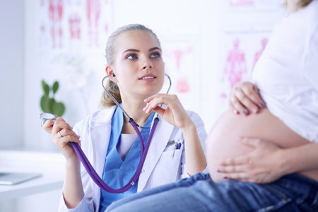 Young woman doctor with stethoscope speaking with pregnant woman at hospital.の写真素材