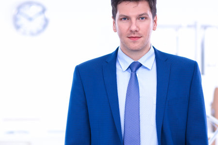 Happy businessman standing in the office in the background working by the deskの写真素材