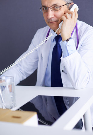 Portrait of senior doctor sitting in medical officeの写真素材
