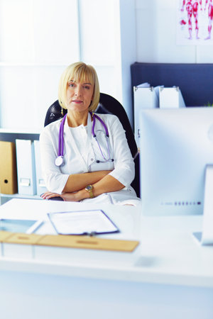 Portrait of young woman doctor in white coat at computerの写真素材