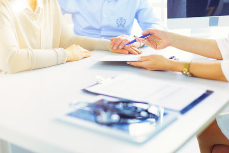 Close up of doctor and patient sitting at the desk near the window in hospitalの写真素材