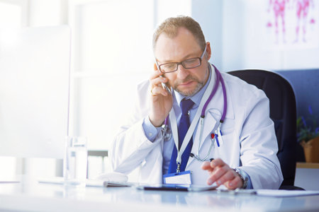 Portrait of senior doctor in office sitting at the deskの写真素材