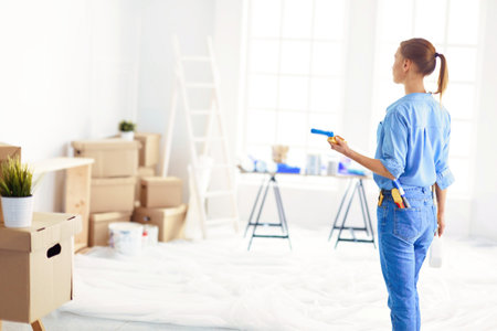 Pretty smilling woman painting interior wall of home with paint rollerの写真素材