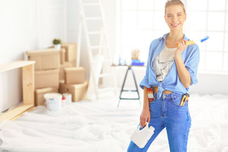 Pretty smilling woman painting interior wall of home with paint rollerの写真素材