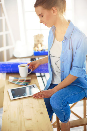Young woman sitting at home and buying new furniture over the Internet using a tablet computerの写真素材