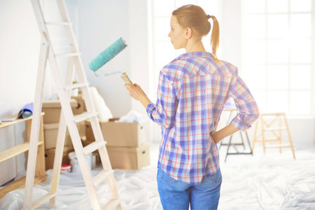 Beautiful young woman doing wall painting, standing near ladderの写真素材