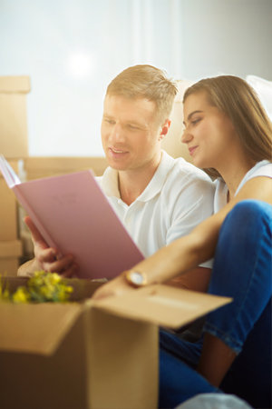 Young couple holding album while sitting on floor in new houseの写真素材