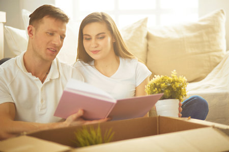 Young couple holding album while sitting on floor in new houseの写真素材