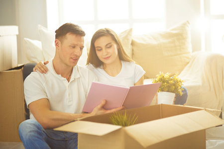 Young couple holding album while sitting on floor in new houseの写真素材