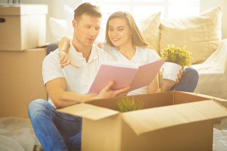 Happy couple looking at photo album while unpacking stuff after relocation to new flatの写真素材