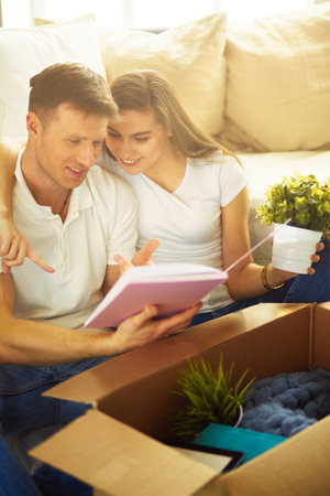 Young couple holding album while sitting on floor in new houseの写真素材