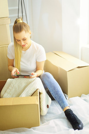 A beautiful single young woman unpacking boxes and moving into a new home. A women look at here tabletの写真素材