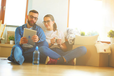 Happy couple planning decoration when moving home sitting on the floorの写真素材