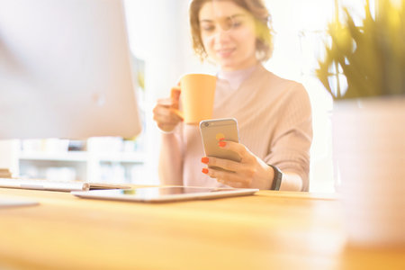 Portrait of beautiful girl using her mobile phone and drinking of coffeeの写真素材