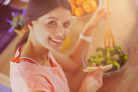 Smiling young woman mixing fresh salad in the kitchen.の写真素材