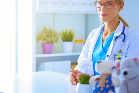 Beautiful young smiling female doctor sitting at the deskの写真素材