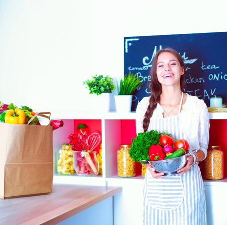 Smiling young woman holding vegetables standing in kitchen. Smiling young womanの写真素材