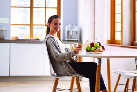 Young woman with orange juice and tablet in kitchen.の写真素材