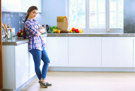 Portrait of young woman standing with arms crossed against kitchen background.の写真素材