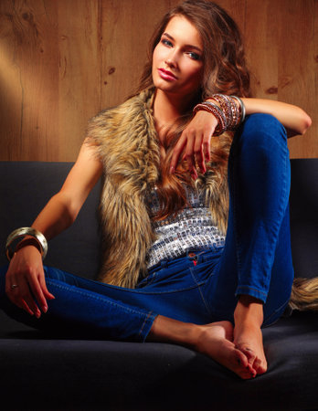 Young beautiful fashion woman in fur coat sitting on the sofa.の写真素材