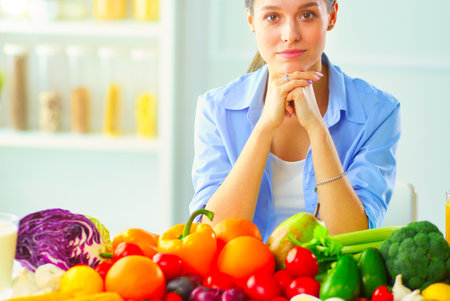 Young and cute woman sitting at the table full of fruits and vegetables in the wooden interior.の写真素材