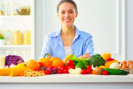 Young and cute woman sitting at the table full of fruits and vegetables in the wooden interior.の写真素材