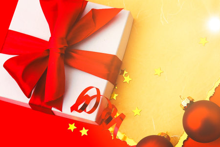 Christmas background or xmas greeting card. White christmas present box with red bow, decorations on red table. Top view with copy space.の写真素材