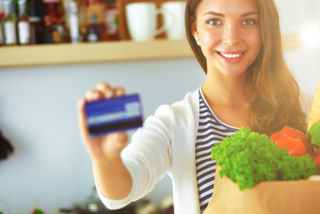 Woman with credit card and shopping bag in the kitchen at homeの写真素材